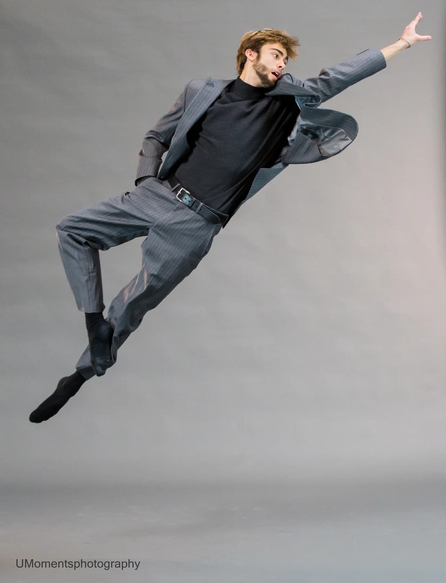 Jeffrey suspended in a lateral jump in a gray suit